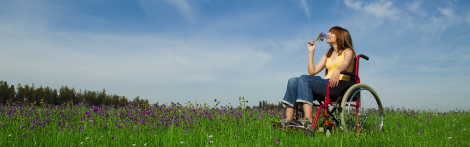 Person in wheelchair in field smelling bouquet of wildflowers.